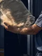 Motion photograph: a heavy sack landing into a man's forearms at a loading bay in morning light, still deforming around the catch