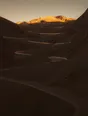 Struck-light photograph: a mountain road climbing in tight switchbacks at dawn with the pass at the top already lit