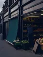 Dark cinematic photograph: An ordinary street of shopfronts under flat grey daylight, one awning wound down.