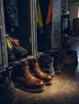 Dark cinematic photograph: One new pair of work boots standing among older, more beaten pairs by a locker.