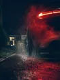 Motion photograph: a car pulling out of a dark driveway in heavy rain at night, tail lights burning through the fall