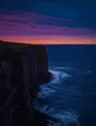 Film photograph: a sheer dark sea cliff with a clean hard edge, waves breaking far below under a plum and teal dusk.
