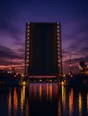 Film photograph: a canal drawbridge raised straight up over dark water at night, its lit edges reflected in the canal.