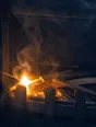 Motion photograph: a match flaring in a cold dark grate at dawn, the kindling just catching and smoke pulling hard up the flue