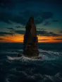 Film photograph: a tall sea stack standing unmoved in rough surf, waves breaking white around its base at dusk.