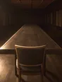 Struck-light photograph: one chair at the head of a very long table, light catching only its back and the table edge