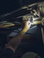 Dark cinematic photograph: An electrician's torch beam finding the fault in a dark ceiling void, one forearm in frame.