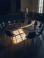 Dark cinematic photograph: A ring of identical chairs set out in a bright hall, none of them at the head.