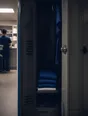 Dark cinematic photograph: A locker door standing open with clean kit folded inside, no name on it.