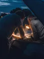 Motion photograph: two men leaning under the raised bonnet of a car at dusk, one holding a light