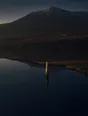 Dawn aerial photograph: a standing stone beside a still mountain tarn, its reflection broken by one ripple ring.