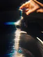 Prism-light photograph: A hand turning a tap full on with water blasting into a sink, hard sun driving through the flow.