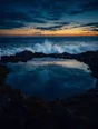 Film photograph: a calm tide pool holding perfectly still water while surf crashes white beyond its dark rock rim.