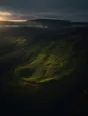 Dawn aerial photograph: an old hillside landslide scar fully regrown in brighter green, a path curving around it.