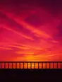 Grainy gradient illustration: A balcony rail facing an enormous magenta and gold sunset, the sun already below the horizon, the sky as the show.