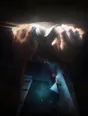 Prism-light photograph: Two chalked hands gripping high on a climbing hold, chalk dust hanging in the hard light.