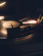 Motion photograph: a record spinning up to speed under one lamp at night, the arm coming across and the rest of the room dark