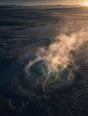 Dawn aerial photograph: a natural hot spring steaming in frosty dawn air, a timber walkway at its edge.