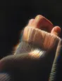 Prism-light photograph: A hand pulling on a knitted jumper, the wool stretching over a wrist in hard sun.