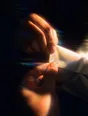 Prism-light photograph: Two hands fastening the button at the cuff of a shirt sleeve, hard sun across the cotton weave.