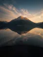 Dawn aerial photograph: a mountain doubled perfectly in a still lake, gold sky above and below, a small wooden dock.
