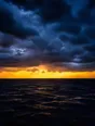 Film photograph: storm clouds breaking open at the horizon over a dark sea, a brilliant band of gold beneath the slate sky.