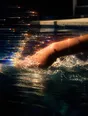 Prism-light photograph: An arm mid-stroke breaking open water, the spray combing hard sun into spectrum.