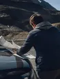 Motion photograph: a man reading a map spread over the bonnet of a car at a high pass, wind tearing at the paper