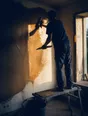 Dark cinematic photograph: A plasterer standing on a low platform working a trowel across a half-skimmed wall at golden hour, the wet plaster catching the low sun.