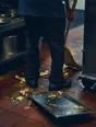 Dark cinematic photograph: A dropped tray being swept up in a bright kitchen, one person's legs and the brush in motion.