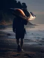 Motion photograph: a man carrying a kayak on his shoulder down a beach at dawn, water still running off it