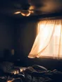Motion photograph: a ceiling fan turning above an unmade bed at first light, the curtain moving at the window