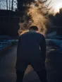Motion photograph: a man bent forward getting his breath back at dawn, steam coming off his shoulders into the cold air