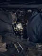 Dark cinematic photograph: A torch beam into an engine bay with exactly two heads bent into it from either side.