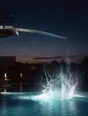 Motion photograph: water exploding upward out of a lit pool at dusk where somebody has just gone in, the high board still flexing