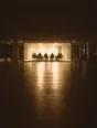Struck-light photograph: one lit glass meeting room seen across a dark empty office floor, the figures around it in silhouette