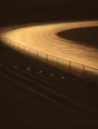 Struck-light photograph: one lit lane of a running track at night, the banked empty seating rising black on both sides