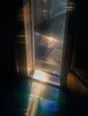 Prism-light photograph: A doorway with rain sheeting past it and hard sun breaking through the shower onto the step.