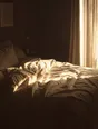 Struck-light photograph: an unmade bed in late morning with the curtains newly pulled open beside it