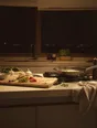 Struck-light photograph: a lit kitchen at three in the morning with the city entirely dark below the window