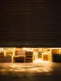 Struck-light photograph: a roller shutter pulled half down over a shop front at midday, the shop lit and working behind the gap