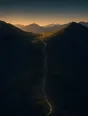 Dawn aerial photograph: a path rising through an open mountain pass toward the sunrise, no one on it yet.