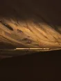Struck-light photograph: one small lit train crossing an enormous empty valley late in the afternoon