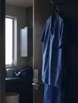 Dark cinematic photograph: A clean pressed uniform hanging on the back of a door in morning light.
