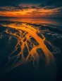 Film photograph: an aerial view of a river braiding into glowing gold channels across dark tidal flats at sunset.