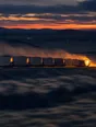 Motion photograph: a long freight train crossing open country at dusk while the land stays sharp