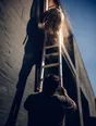 Motion photograph: a man holding a ladder steady at the base while another works high on it at midday