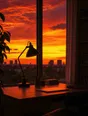 Film photograph: a desk lamp switched off on a tidy desk beside a window blazing with crimson and gold sunset.
