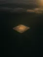 Dawn aerial photograph: green crop rows with one deliberate unsown square, morning light pooling in the open space.