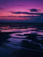 Film photograph: a wide tidal flat at dusk, the sea drawn back into mirror pools under one huge plum and teal sky.